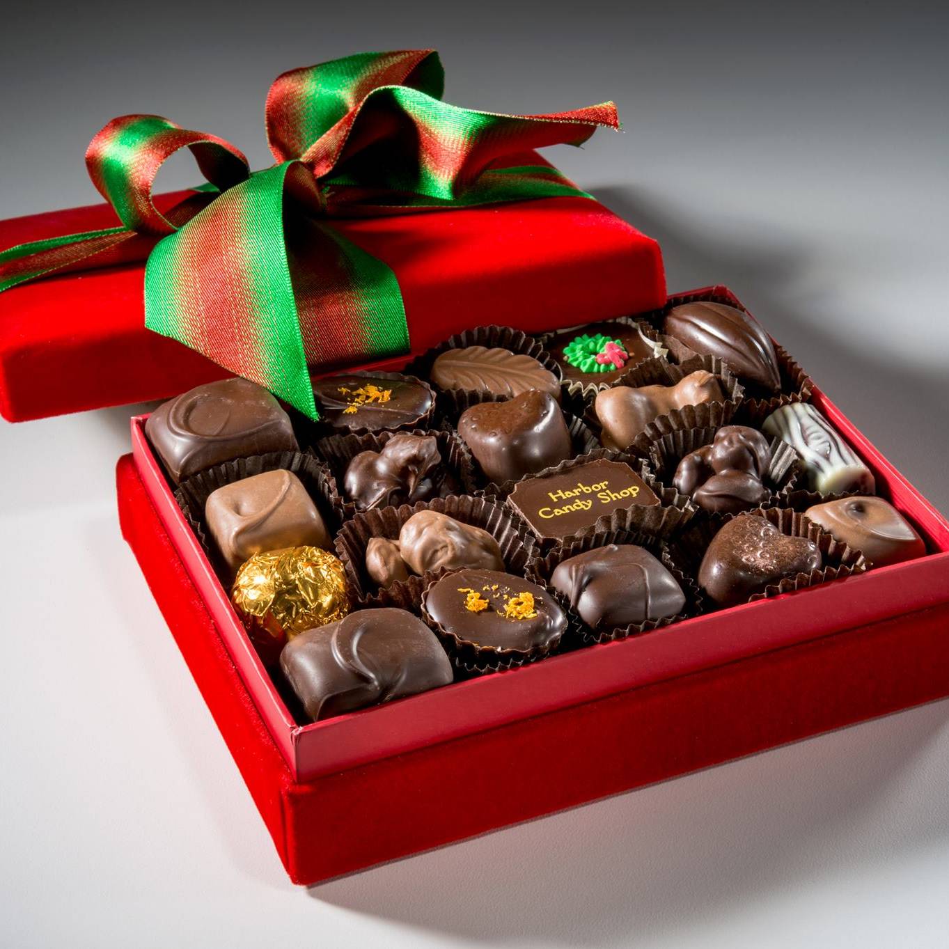 A box of chocolate in a red decorative box with red and green ribbon