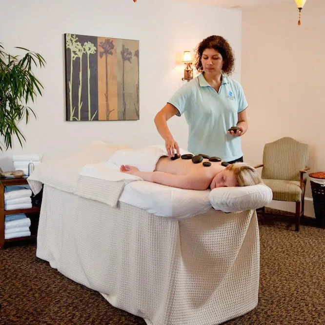 A woman laying on a massage table receiving a stone massage.