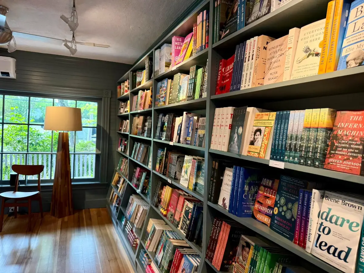 The interior of Perkins Cove Bookshop, with shelves of books and a lamp in front of a window.