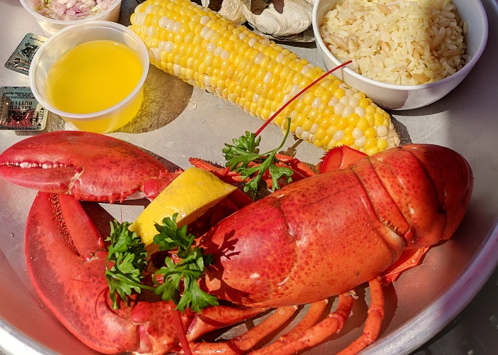 A cooked lobster on a plate with corn, butter and rice
